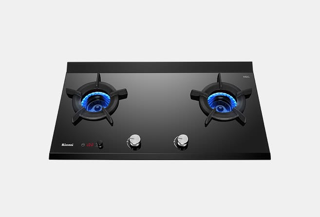 Black two-burner gas stovetop with blue flames and two control knobs at the front, on a light gray background, brand name visible in corner.