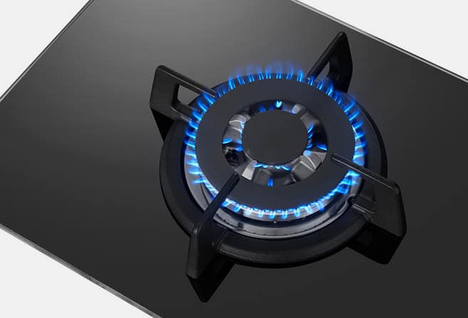 Black glass gas cooktop with a single burner lit by blue flame and a control knob nearby