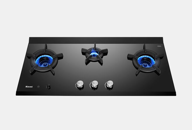 Black glass gas cooktop with three burners and stainless steel control knobs in the center, blue flame lit on each burner, Rianni brand logo visible on left.