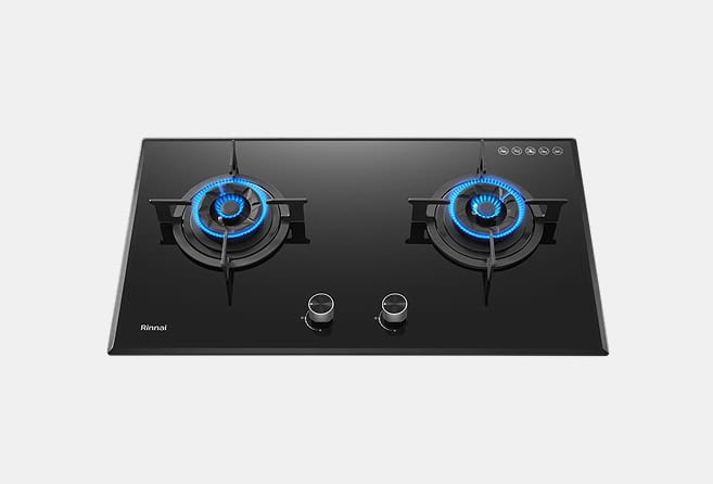 Black glass gas cooktop with two lit burners showing blue flame rings and two control knobs (Rinnai brand)./Two-burner gas stove on a glossy black surface with blue flames and chrome knobs.