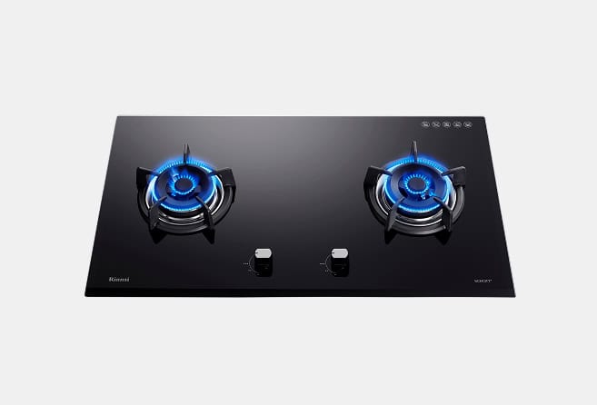 Black glass two-burner gas cooktop with blue flames on each burner and centered control knobs.