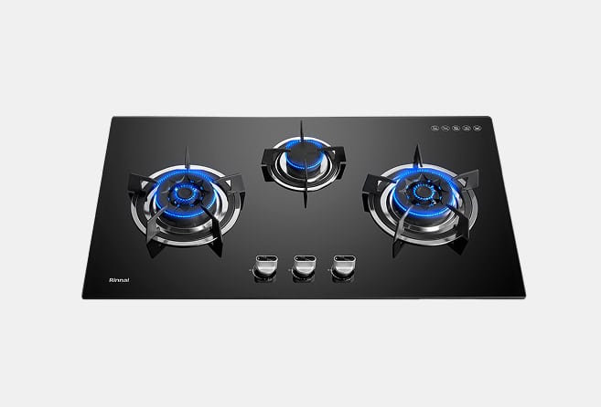 Black glass gas cooktop with three lit burners and blue flames; control knobs centered below the burners.