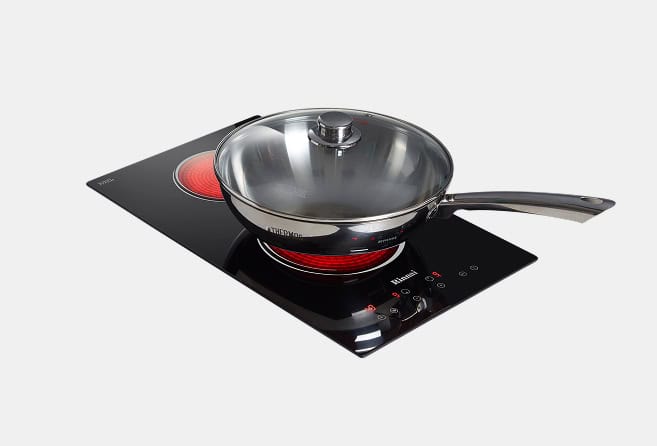 Frying pan with glass lid on a black induction cooktop with red heating coils visible underneath
