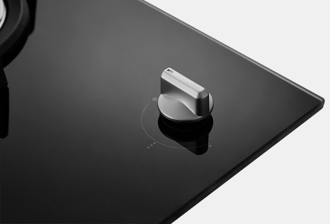 Close-up of a modern metal control knob on a glossy black glass induction cooktop surface.