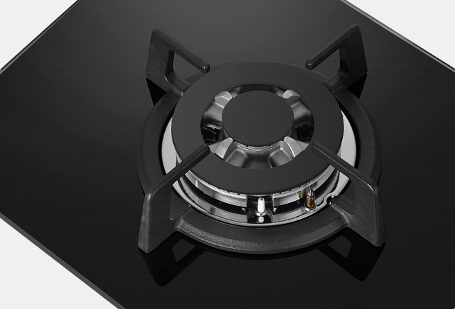 Gas stove burner on a black glass surface, showing the ring and support grates with a visible ignition and burner ports.