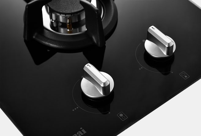 Close-up of a black glass gas stove with two silver knobs and a burner.