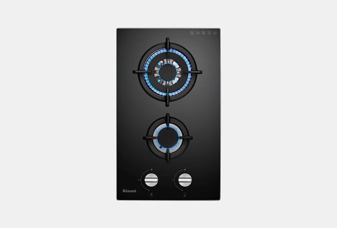 Black glass gas stove with two lit burners emitting blue flames and four control knobs at the bottom (Rinnai).