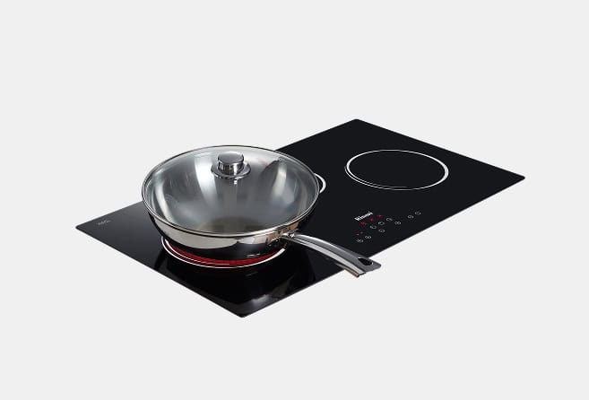 Stainless steel wok with a glass lid on a black glass-ceramic induction cooktop.