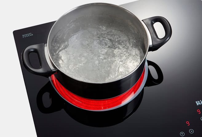 Pot with boiling water on a black glass electric stove burner, red-hot ring visible beneath the pot edge