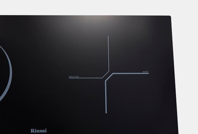 Close-up of a black control panel with a blue schematic showing induction and boost lines converging at a central junction; Rinnai logo bottom left.