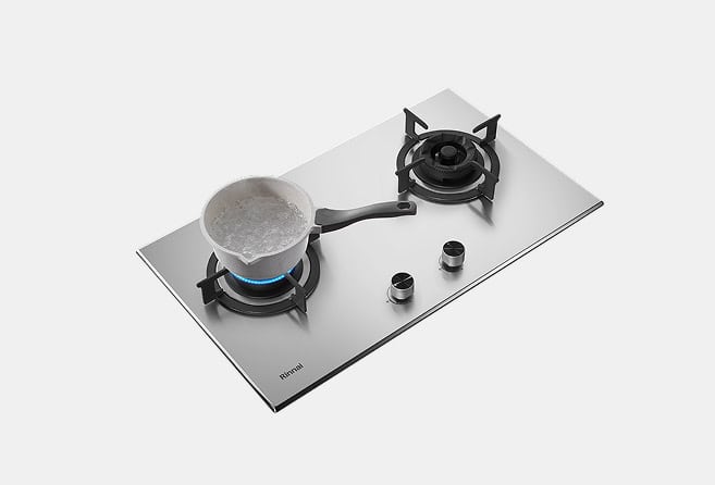Stainless steel gas cooktop with two burners; left burner lit with a blue flame and a pot boiling on it.