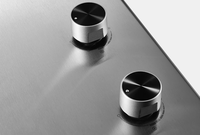 Two metal stove knobs on a brushed stainless steel surface viewed from above with indicator marks nearby.