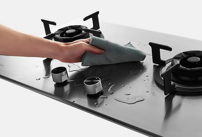 Person cleaning a stainless steel gas stove top with a cloth, wiping around the burners.