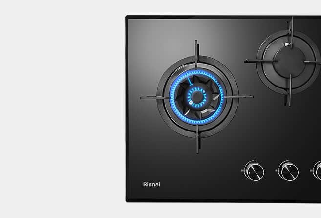 Black gas cooktop with a glowing blue flame on the left burner and control knobs on the right side (Rinnai).