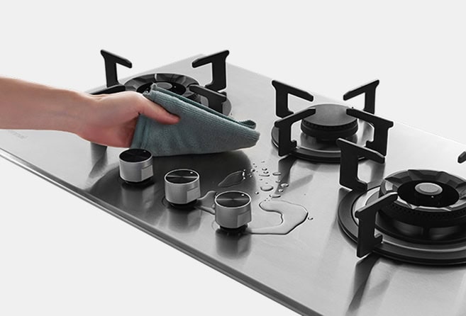 Person cleaning a stainless steel gas stove with a green cloth on the cooktop area