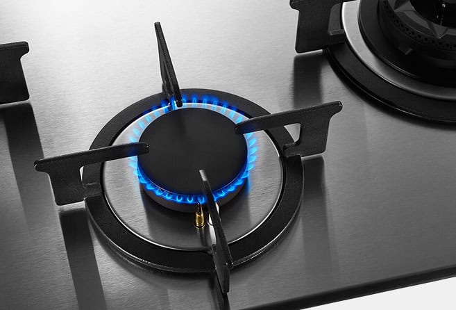 Close-up of a lit gas burner with a blue flame on a stainless steel stovetop.