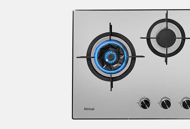 Stainless steel gas cooktop with two burners; left burner lit with a blue flame and control knobs visible below.