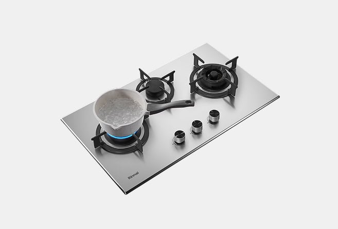 Stainless steel gas cooktop with three burners; a silver pot on the left burner over a blue flame, and four control knobs in front.