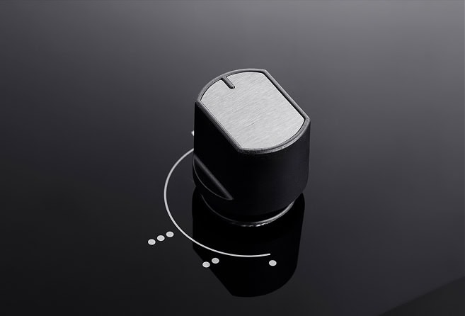 Close-up of a black and silver rotary control knob on a glossy dark surface, with a circular alignment mark nearby.
