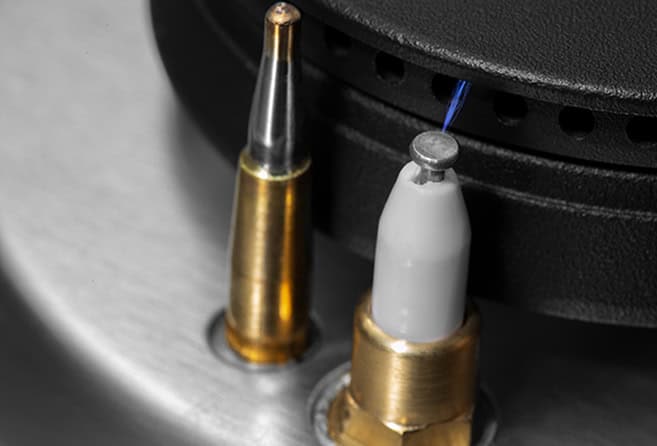 Close-up of a vinyl turntable needle (stylus) and cartridge with a blue wire visible on a metal surface.
