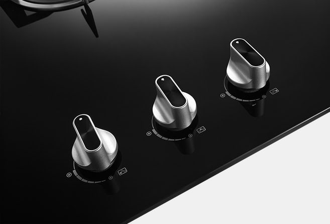 Three metal stove knobs on a glossy black cooktop, arranged in a row from left to right.