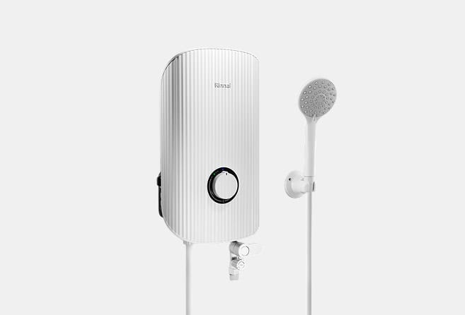 White vertical electric shower heater with a circular control dial and a connected handheld shower head on the right, mounted on a wall edge outlet hose below.