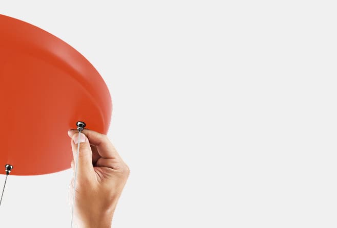 Close-up of a hand tying the string to a red balloon against a pale background.