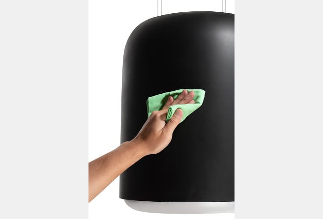 Person’s hand wiping a glossy black cylindrical surface with a green microfiber cloth, cleaning action