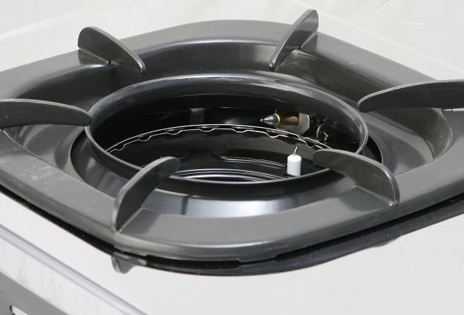 Close-up of a gas stove burner with a black metal grate and exposed inner burner ring.