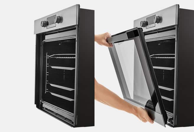 Hands lift a glass oven door away from a black wall oven, exposing the empty racks inside.