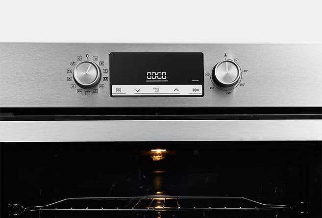 Stainless steel oven with a digital control panel and two knobs, interior rack visible and the oven light on.