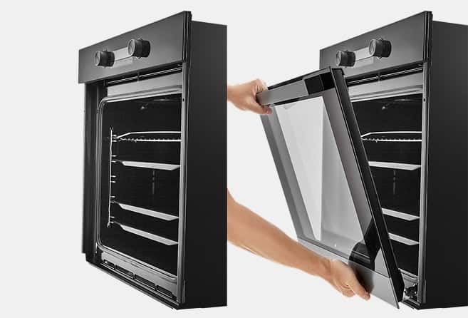 Two black built‑in ovens with a person removing the right oven's glass door for cleaning.