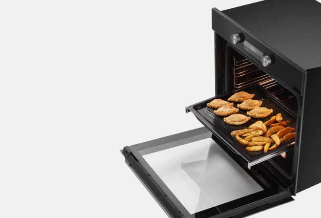 Compact oven with the door open, showing a baking tray of golden-brown pastries inside.