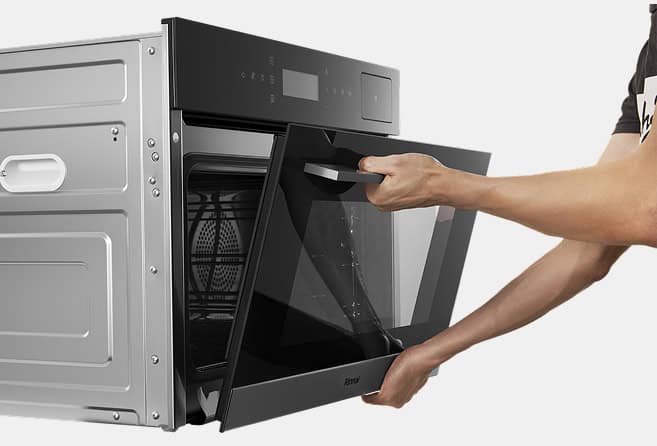 Hands open a stainless steel wall oven with a glass front; interior rack visible.