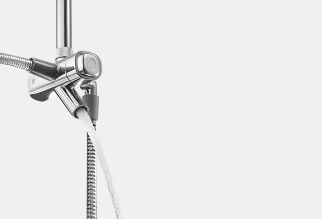 Chrome shower mixer with handheld spray head and flexible hose attached to a vertical rail in a bright bathroom setting.