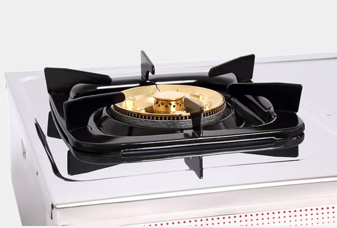 Close-up of a brass gas burner on a white enamel stovetop with black grates