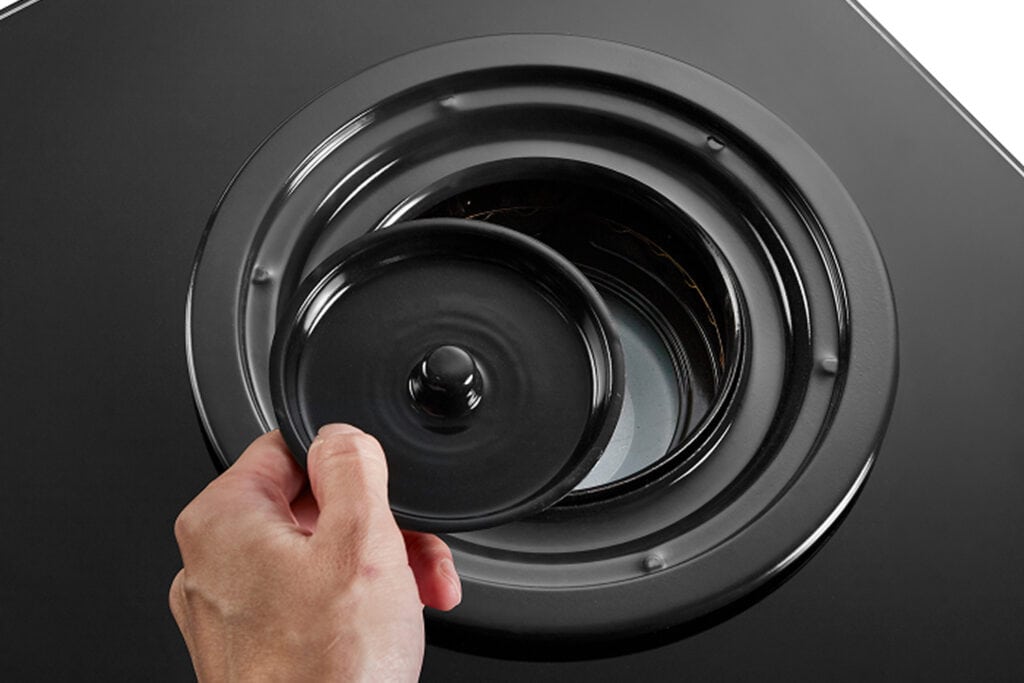 Hand removing the dust cap from a large speaker driver.