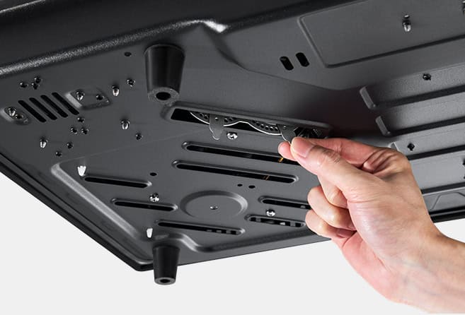 Close-up of a hand removing or inserting a component inside a computer chassis, showing a slot and metal interior plate under a device's underside